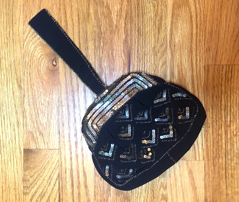 May include: A black evening bag with a gold and silver sequined design. The bag has a long black strap.