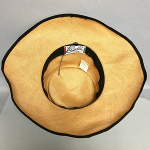 May include: A wide-brimmed straw hat with a black ribbon around the edge. The hat has a label that reads "New York Paris London" and "Classic".