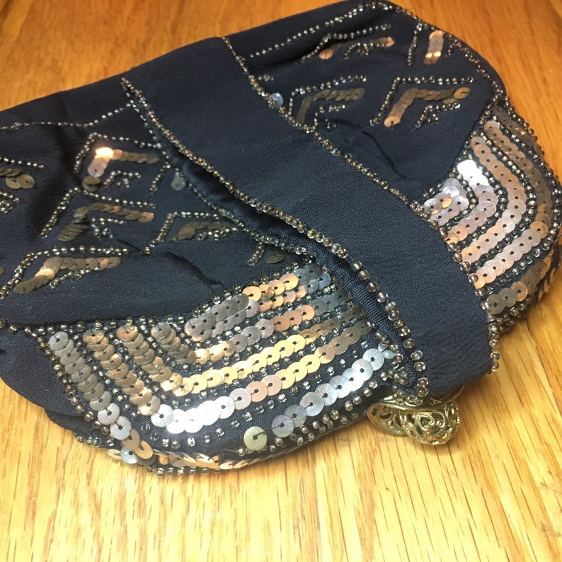 May include: A black sequined evening bag with a gold clasp. The bag is decorated with silver and gold sequins in a geometric pattern.