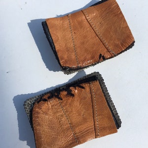 May include: Two brown leather wrist cuffs with metal rivets and black stitching.