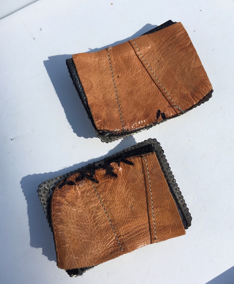 May include: Two brown leather wrist cuffs with metal rivets and black stitching.