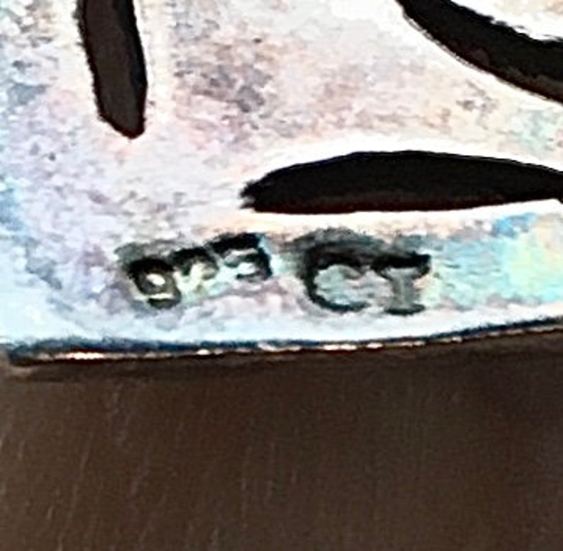 May include: Close-up of a silver charm with the inscription "925 CI" on the back.
