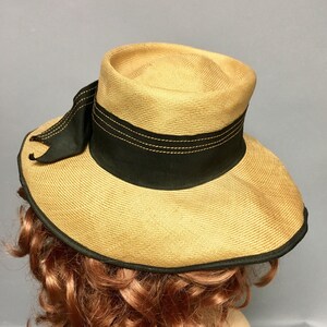 May include: A straw hat with a wide brim and a black ribbon around the crown. The hat has a black ribbon with a bow on the side.