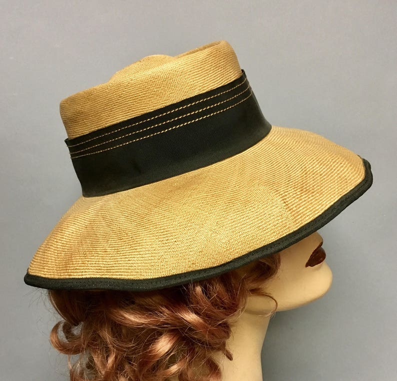 May include: A wide-brimmed straw hat with a black ribbon and a gold trim. The hat has a slightly rounded crown and a wide, floppy brim.