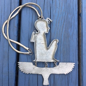 May include: Silver necklace with a pendant featuring a stylised figure of a person sitting on a bird with outstretched wings.