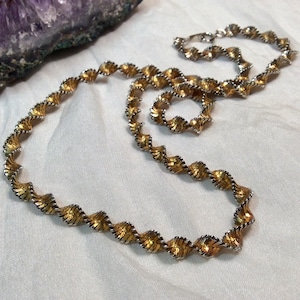 Peut inclure: Un collier bicolore présentant un design en spirale continu. La chaîne est composée de segments alternés de métal doré et argenté poli, créant un aspect de corde torsadée texturée sur toute la longueur de la pièce de bijouterie.
