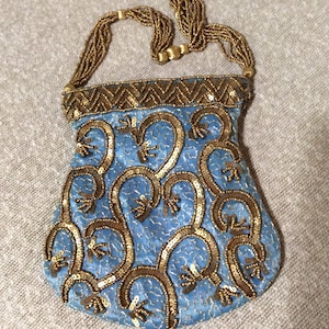 Puede incluir: Un bolso de mano vintage azul claro con un asa y ribete de cuentas doradas. El bolso presenta un diseño repetido de lentejuelas doradas. El asa está hecha de múltiples hilos de cuentas doradas.
