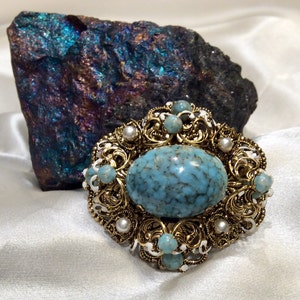 May include: A large oval turquoise cabochon set in a gold filigree brooch with white and turquoise accents.