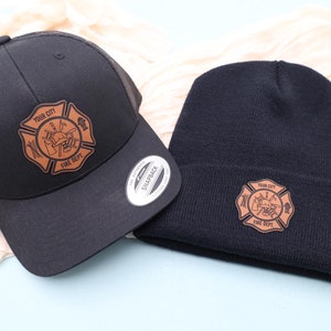 May include: A black trucker hat and a black beanie with a brown leather patch featuring a firefighter's helmet, axe, and hose with the text "YOUR CITY FIRE DEPT."