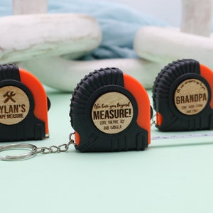 May include: Three personalized tape measures with wooden inserts. The first tape measure says "Dylan's Tape Measure" with a hammer and wrench symbol. The second tape measure says "We love you beyond measure! Love, Balpre, Aly and Isabella". The third tape measure says "Grandpa".