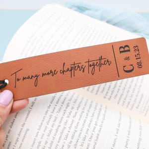 Pode incluir: Um marcador de página de couro castanho com o texto "To many more chapters together" e as iniciais "C & B" com a data "08.15.23".