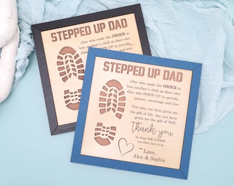 May include: Two wooden signs with blue and black frames. The signs have a wood grain background and feature the text "Stepped Up Dad" with a quote about the importance of a stepparent. The signs also feature a cutout of a footprint.