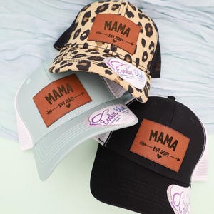 Pu&ograve; includere: Tre cappellini da camionista con la scritta "MAMA" su una toppa in pelle marrone. Un cappellino ha una stampa leopardata, un altro &egrave; azzurro e il terzo &egrave; nero. Ogni cappellino ha un retro in rete e una visiera curva.