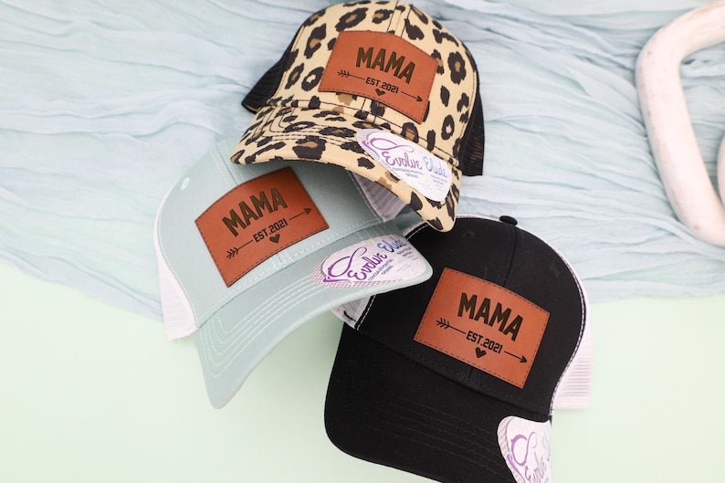 Pu&ograve; includere: Tre cappellini da camionista con la scritta "MAMA" su una toppa in pelle marrone. Un cappellino ha una stampa leopardata, un altro &egrave; azzurro e il terzo &egrave; nero. Ogni cappellino ha un retro in rete e una visiera curva.