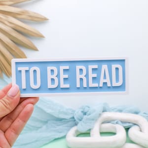 May include: A light blue rectangular sign with white trim and the text "TO BE READ" in white letters.