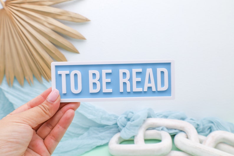 May include: A light blue rectangular sign with white trim and the text "TO BE READ" in white letters.