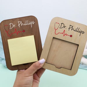 May include: Two wooden memo boards, one with a dark brown finish and the other with a natural wood finish. Both feature the name "Dr. Phillips" in script, a red stethoscope graphic, and a red heartbeat line. One board has a yellow sticky note pad.