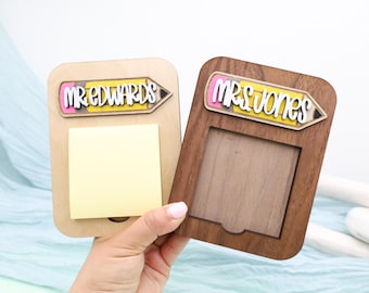 May include: Two wooden desk organizers, one light-colored and one dark-colored. The light-colored organizer has a yellow sticky note pad and the text "MR.EDWARDS" in a pencil-shaped design. The dark-colored organizer has the text "MRS.JONES".