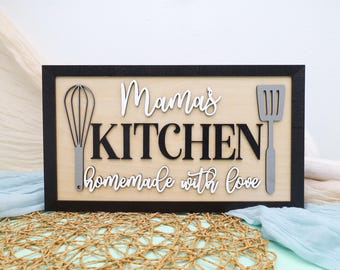 May include: A wooden sign with black lettering that reads "Mama's Kitchen homemade with love". The sign is decorated with a silver whisk and spatula.