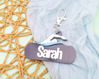 May include: A gray and white personalized keychain with a swimmer silhouette and the name "Sarah" on a black background.