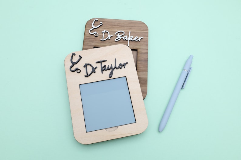Pu&ograve; includere: Due cornici in legno con un'icona di stetoscopio e il testo "& Dr. Baker" e "& Dr. Taylor" su uno sfondo verde chiaro. C'&egrave; anche una penna blu chiaro nell'immagine.