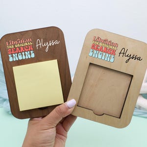 May include: Two wooden memo holders, one dark brown and one light brown, with the text "Librarian the Original Search Engine" and the name "Alyssa". The dark brown holder has a yellow sticky note.