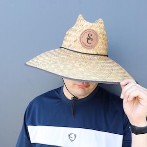 Pode incluir: Uma pessoa usando um chap&eacute;u de palha com um remendo de couro marrom que diz "S&C". O chap&eacute;u tem uma aba larga e est&aacute; puxado sobre os olhos da pessoa. A pessoa est&aacute; usando uma camisa listrada azul e branca.