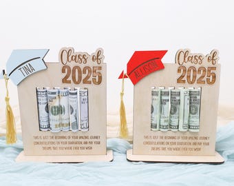 May include: Two wooden graduation money holders with a graduation cap design. The holders are personalized with the names "Tina" and "Allison" and the year "2025". Each holder has slots for rolled bills and a message that reads "This is just the beginning of your amazing journey. Congratulations on your graduation, and may your dreams take you wherever you wish."