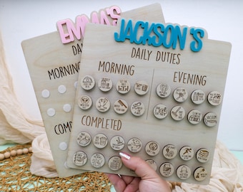 May include: Wooden daily duties chart with the name "Jackson's" in blue letters. The chart has sections for morning and evening tasks, with small wooden tokens illustrating various activities. The word "Emma's" is on a similar chart.