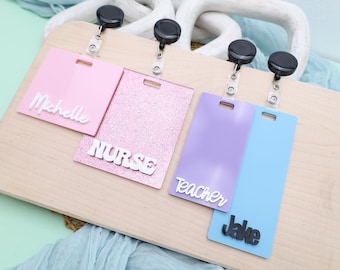 May include: Four different colored acrylic badge holders with retractable badge reels. The holders have the words "Michelle", "Nurse", "Teacher", and "Jake" written on them.