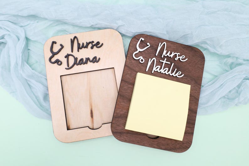 Pu&ograve; includere: Due porta-appunti in legno con un design a stetoscopio e il testo "Nurse to Diana" e "Nurse to Natalie". Un porta-appunti ha un post-it vuoto e l'altro ha uno spazio vuoto per una foto.