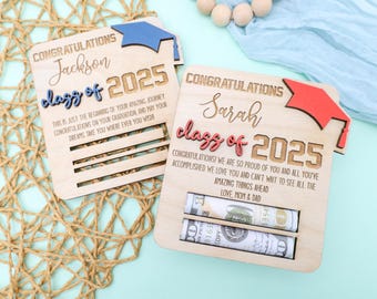May include: Two wooden graduation money holders with slots for cash. The top of each holder has a graduation cap. The first holder is blue and says "Congratulations Jackson Class of 2025". The second holder is red and says "Congratulations Sarah Class of 2025".