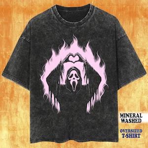 May include: Dark gray mineral washed oversized t-shirt featuring a pink graphic of the Ghostface mask from the Scream movie franchise. The graphic includes a heart shape formed by hands and flames. The text "MINERAL WASHED" and "OVERSIZED T-SHIRT" are printed on the bottom right.