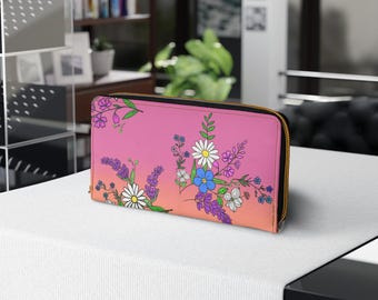 Op de afbeelding: Een roze en oranje bloemenprint portemonnee met een zwarte rits. De portemonnee heeft verschillende bloemen in tinten roze, wit, blauw en paars.