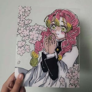 Puede incluir: Una lámina acrílica transparente con una colorida ilustración estilo anime de un personaje con largo cabello trenzado rosa y amarillo, vistiendo un uniforme blanco y negro, comiendo un pequeño alimento redondo, rodeado de flores de cerezo rosas.