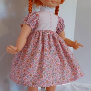 May include: A red-haired doll wearing a pink and white floral dress with black shoes. The doll has braids and blue eyes.