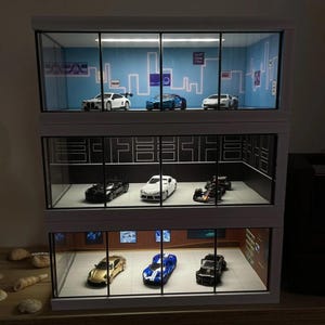 May include: A three-tiered glass display case with a white frame. The case is filled with miniature toy cars, including a black and white race car, a white sports car, a black sports car, a gold sports car, a blue sports car, and a blue and white sports car.
