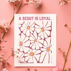 May include: A white card with pink flowers around it. The card has a pink daisy pattern and the text "A SCOUT IS LOYAL."