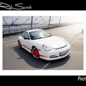 Puede incluir: Un coche deportivo Porsche blanco con llantas rojas y detalles laterales. El coche está aparcado sobre una superficie de hormigón. El texto "GT3 RS" es visible en el lateral.