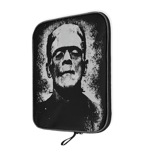 Op de afbeelding: Zwart-grijze etui met ritssluiting met een verweerde afbeelding van Frankenstein's monster. Het ontwerp is een grijswaardenportret met zichtbare steken in de nek. De etui heeft een zwarte ritssluiting en een kleine lus.