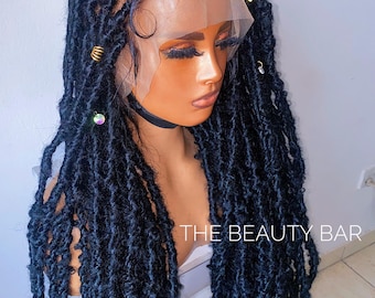 May include: A black lace front wig featuring long, textured faux locs with a matte finish. The hair is styled with gold-toned metal hair cuffs and small decorative beads. The text THE BEAUTY BAR is visible on the lower right side of the image.