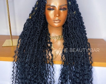 May include: A long, black, textured wig with distressed locs and loose, curly ends. The wig features a lace front with baby hairs, gold-colored decorative thread accents, and small metallic hair cuffs. The text THE BEAUTY BAR is visible.