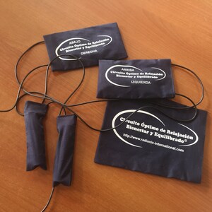 Puede incluir: Un conjunto de almohadillas y mangos de relajación azul marino conectados por cables negros. Las almohadillas tienen texto blanco que dice "Circuito Óptimo de Relajación Bienestar y Equilibrado" y etiquetas direccionales. También se ve una dirección web.