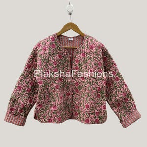 Peut inclure: Veste matelassée rose avec un motif floral de fleurs rouges et de feuilles vertes. La veste a des manches longues, deux poches et un col rond. Le texte "LakshaFashions" est visible sur la veste.