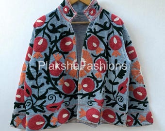 May include: A light blue jacket with intricate floral embroidery in red, orange, and green. The jacket features a high collar and is displayed on a wooden hanger. The brand name "Plaksha Fashions" is visible.