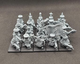 May include: A collection of gray miniature figurines, likely for tabletop gaming. The figures are detailed with ornate hats, weapons, and a banner. They are arranged on individual square bases, suggesting a strategic game.
