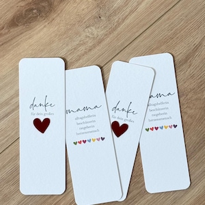 Könnte beinhalten: Vier weiße rechteckige Karten mit abgerundeten Ecken, jede mit Text und einem Herz. Die Karten haben die Wörter "danke" und "mama" in handschriftlichem Stil, zusammen mit anderem Text und einem roten Herzen. Die Karten liegen auf einer Holzoberfläche.