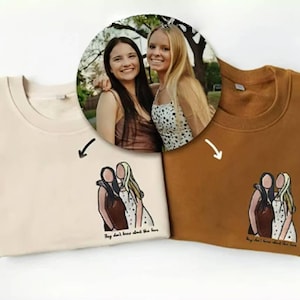 Op de afbeelding: Twee bruine T-shirts met een witte en bruine illustratie van twee vrouwen met de tekst "They don't know about the love" gedrukt op de onderkant.