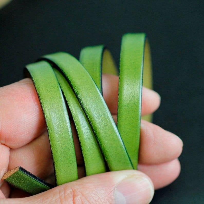 May include: Close-up of a green leather cord, folded and held in a hand. The leather has a smooth, polished finish.