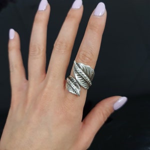 May include: A silver ring featuring a design of two leaves, each with a row of small beads. The ring is adjustable and can be worn on different fingers.
